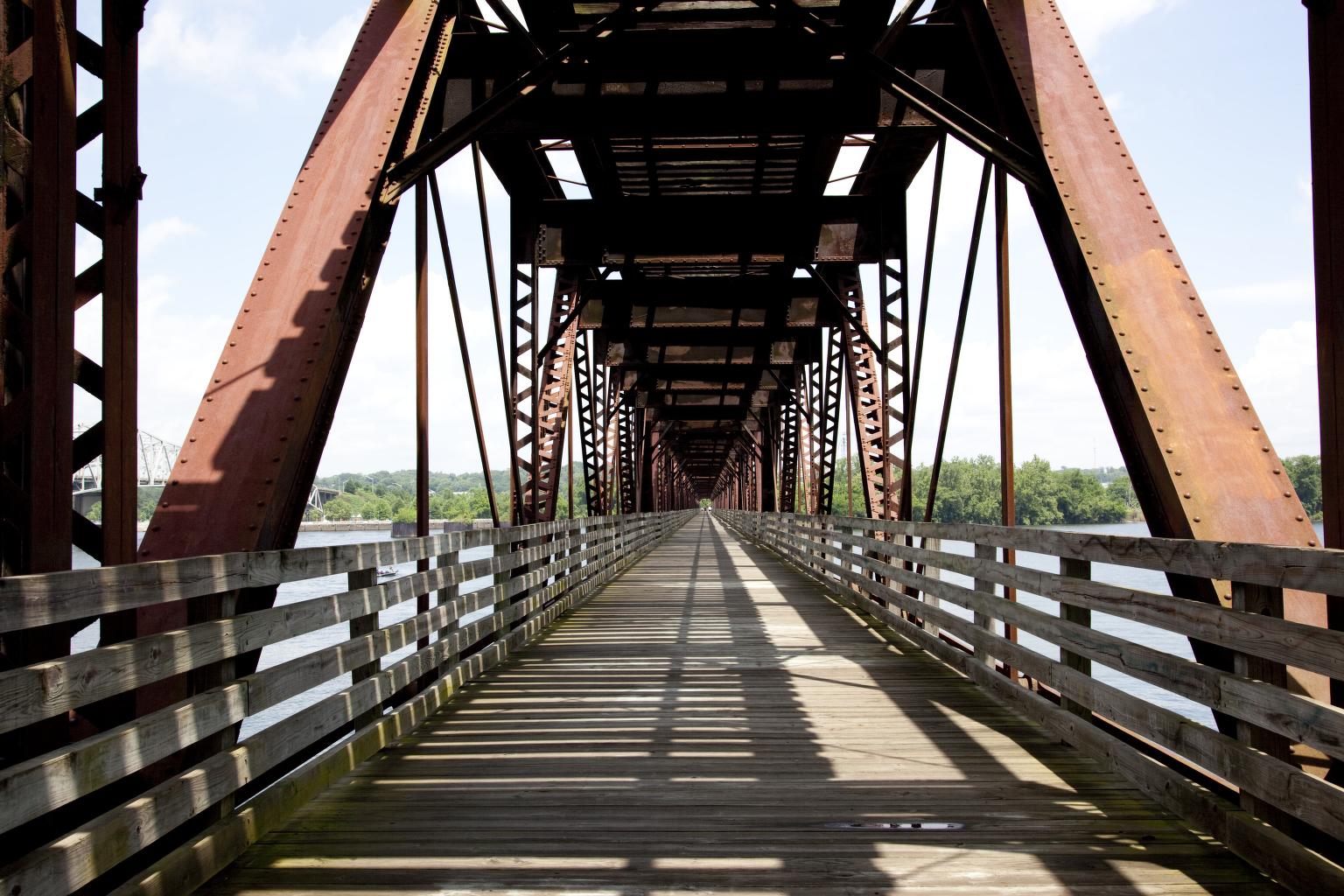 A 2010 view along the Old Railroad Bridge’s wooden lower walkway, with railings, steel beams overhead and the river beside it